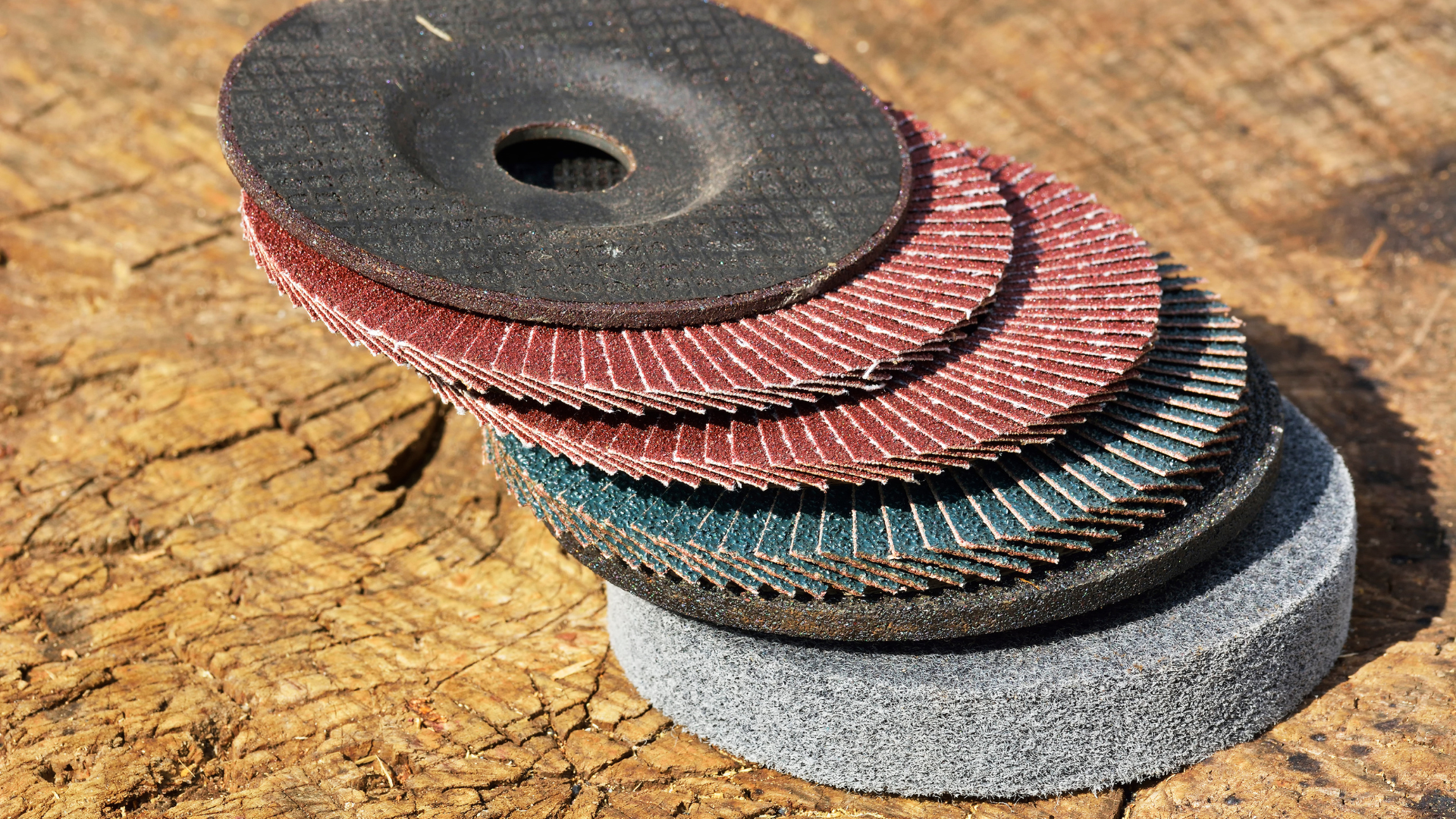 A stack of various colored sanding discs for an angle grinder, resting on wood.