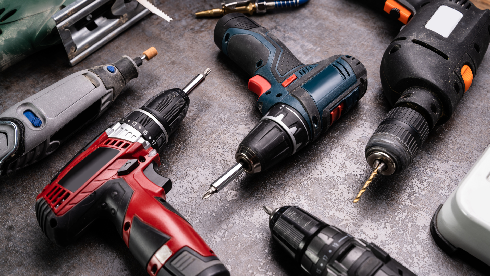 Assortment of power tools, including drills and a rotary tool, arranged on a textured surface.