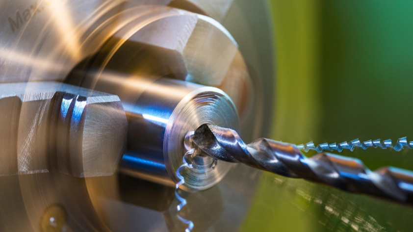 A drill bit cutting into metal on a lathe, creating metal shavings.