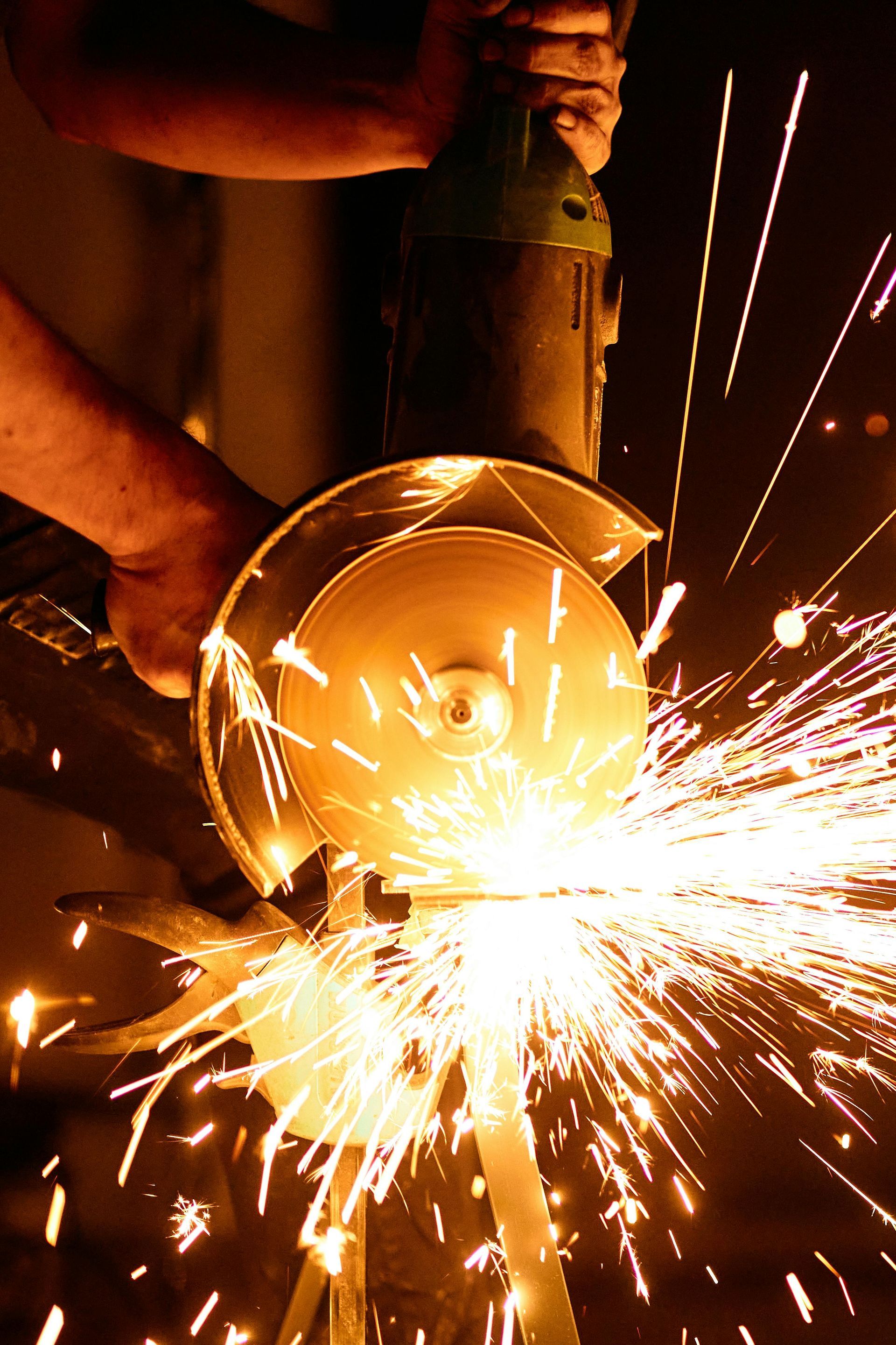 Person using a power grinder, creating sparks while working on metal in a workshop.
