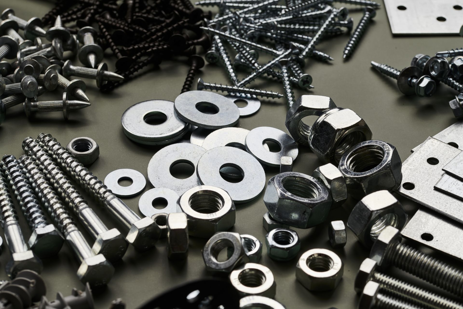 Close-up of various metal hardware: screws, nuts, bolts, and washers arranged on a surface.